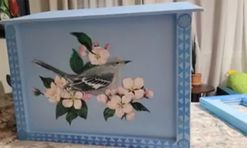 Blue Plaza Frida bookshelf with hand painted birds and flowers near the soccer field entrance.